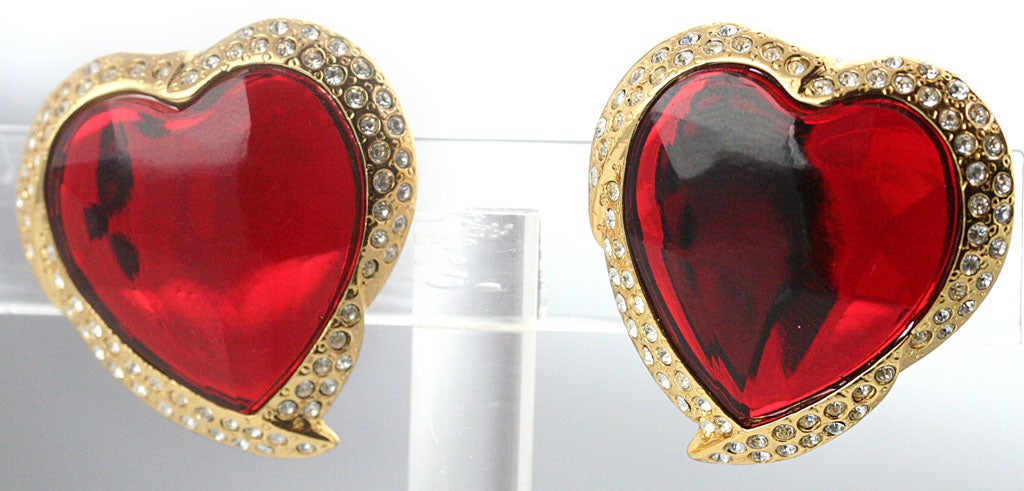 A whimsical pair of heart shaped ear clips by YSL with a sparkling red heart center set in gold plated metal inset with rhinestones.