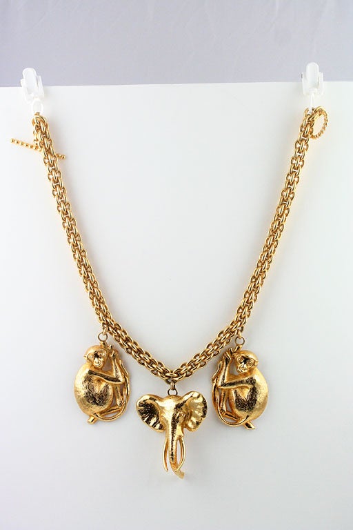 A striking gold tone chain necklace by Dominique Aurientis with a pair of of large-scale monkey charms and an elephant charm dangling from it. Each of the charms is marked 