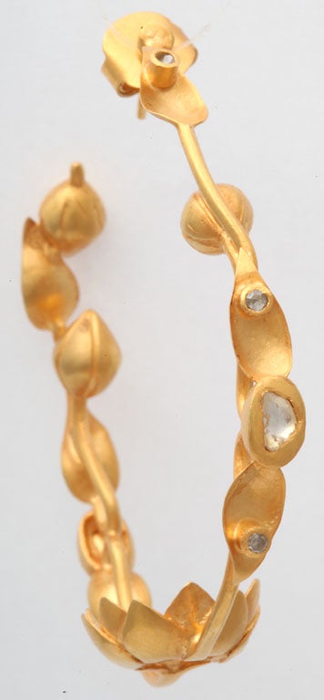 A pair of 18kt yellow gold lotus flower hoops. The earrings are composed of an 18kt yellow gold vine adorned with lotus flower buds and leaves and have scattered rose cut diamonds scattered throughout the vine. There are also rose cut diamonds set