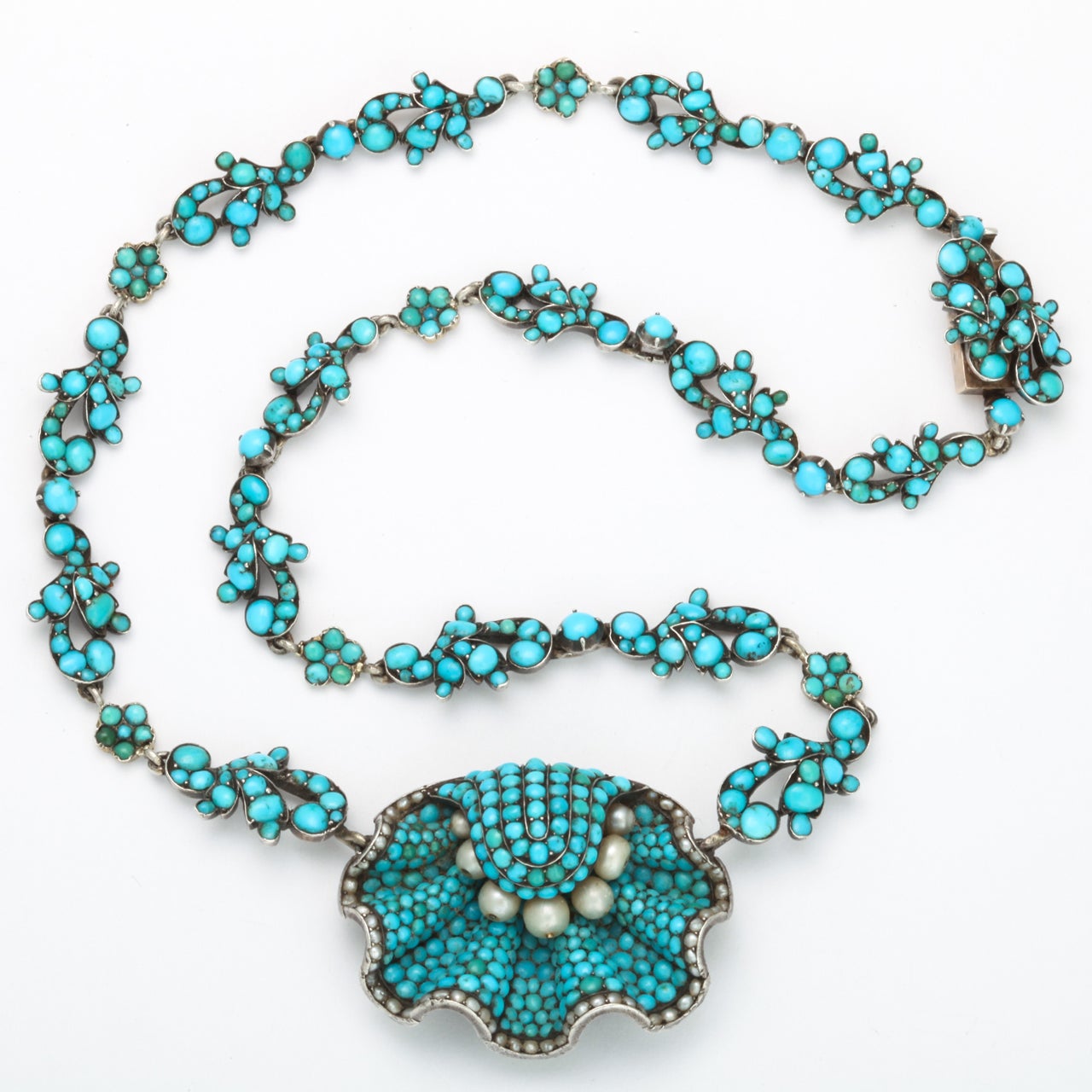An astounding necklace designed with a garland of turquoise flowers that bring center stage a scallop shell bearing seven natural pearls. The workmanship is sublime, actually breathtaking.
The shell, completely encrusted with natural pave