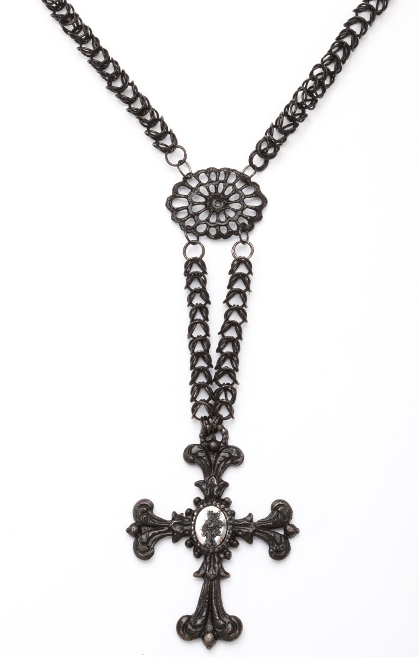 The Georgian Berlin Iron Chain, composed of intricate interlocking links. drops nine inches from the clasp top section and 14 inches over all to the bottom of the ornamental cross, falling to the top of the breast. This top section is separated from