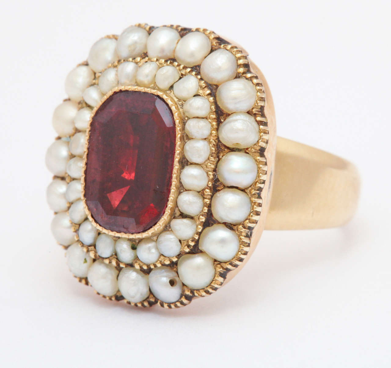 Scalloped edges frame two rows of natural pearls in a Georgian ring of 18kt gold c. 1820. The center garnet, a squared rectangle, is a luscious red set with generous prongs that give texture to the jewel. The stone is set in a closed back setting