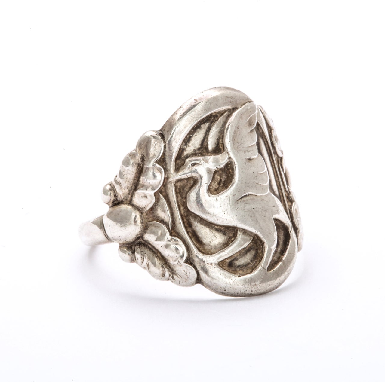 A 1930's Georg Jensen Silver Ring is engraved with the image of a powerful bird  with a smile in its eye. The bird is possibly a griffon that appears to have just landed from flight.  The shoulders of the ring are detailed with large chased or