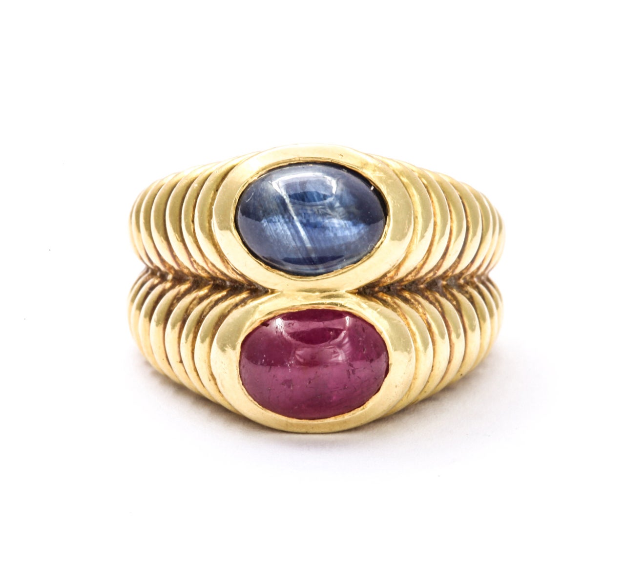 A fashionable double band ring of 18 kt gold  that elegantly sits raised from the finger. The gold band forms two pyramids that  are engraved in concentric rings. Atop in oval frames  sit  a sapphire and a ruby. The ring proportions are wearable and