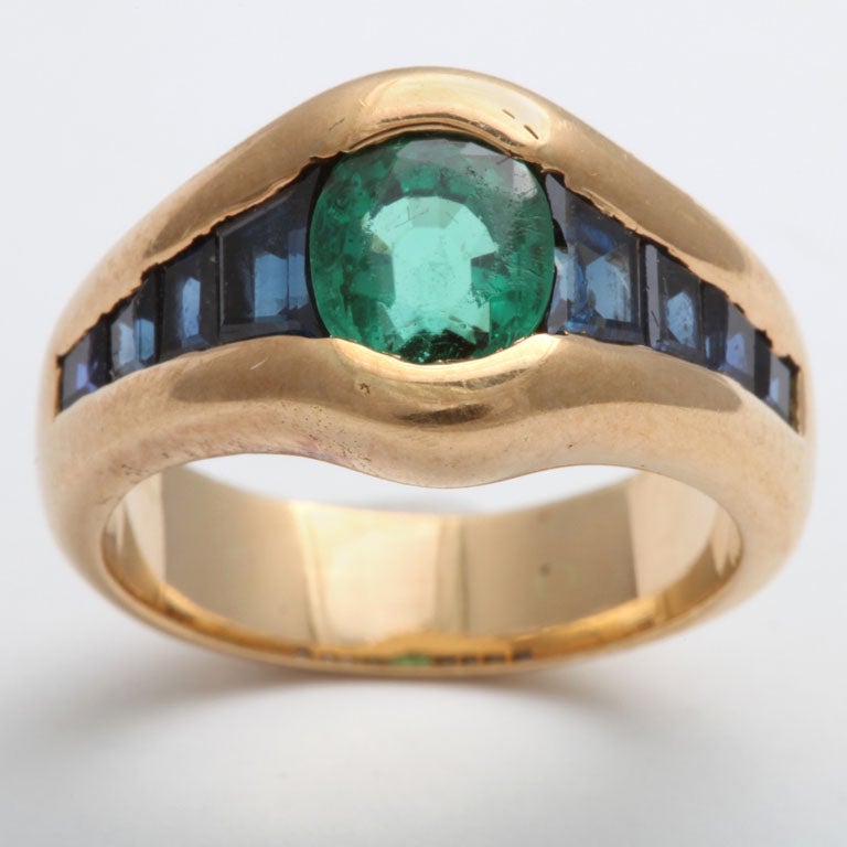 Oval Faceted Emerald invisibly set with sumptuous graduated Calibre Cut Sapphires
Set in 18kt Yellow Gold. Size 4 1/2.  Can be made slightly larger.