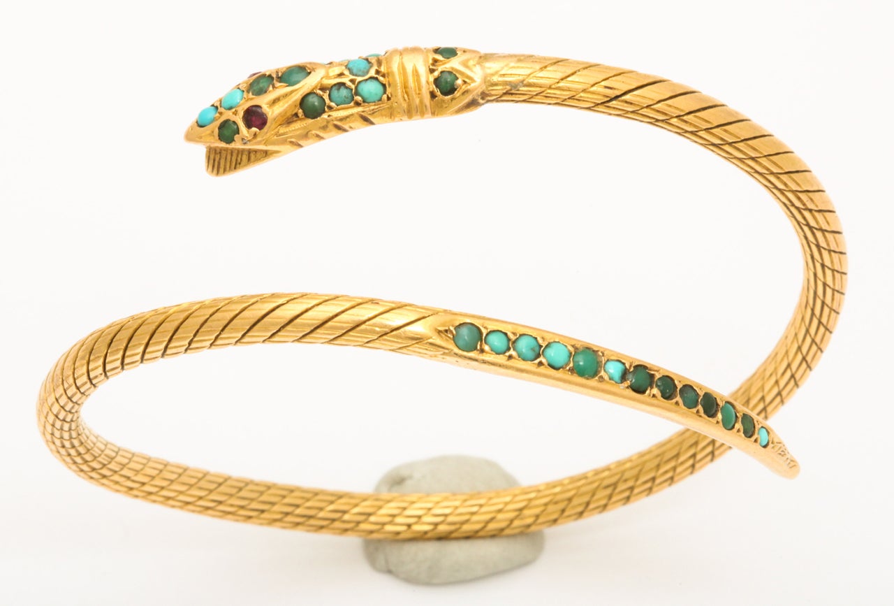 A fabulous 18 kt solid gold Egyptian Revival hand chased coiled snake bracelet with turquoise set stone decorations with ruby eyes. Adjustable size.