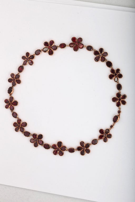 A superior necklace of love poesies set with sparkling red, Georgian flat cut, foiled garnets in 15kt gold forms a wreath around the neck, or alternatively separate to make a bracelet for each wrist. The flowers, forget-me-nots, literally mean ;I am