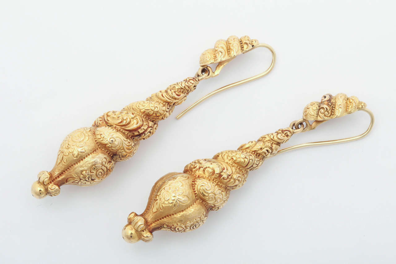 Suggestive of a serpent curled around flowers, this pair of 15 kt gold Victorian chandelier earrings originate from England in c.1840.  The unusual coiled design is lushly engraved with flowers and granulation and emanates the lush fertility of all