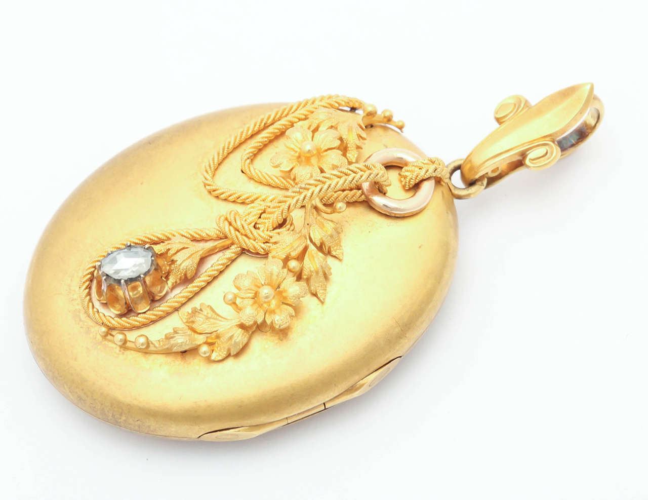 This large oval locket in 14kt gold presents a rare design that projects passion and sentiment. Draped over the face is a cord or rope that passes through a gold ring. Midway down the locket, the cord is knotted. As in a love knot, which is the