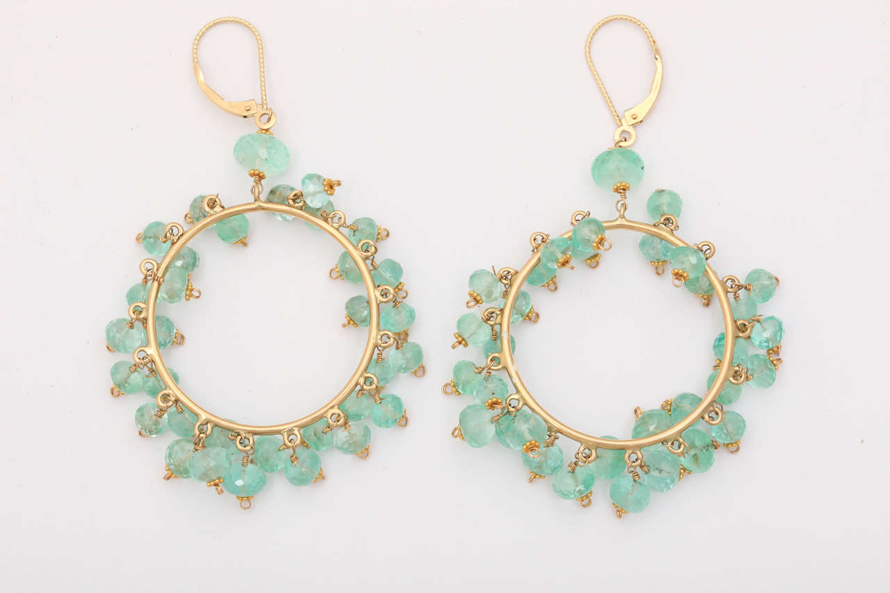 These spectacular earrings are  faceted, light green emerald beads dangling playfully from gold hoops .The eurowires keep these dynamic earrings secure as they sparkle with your every move. Holding each emerald bead is an 18 kt rosette. These