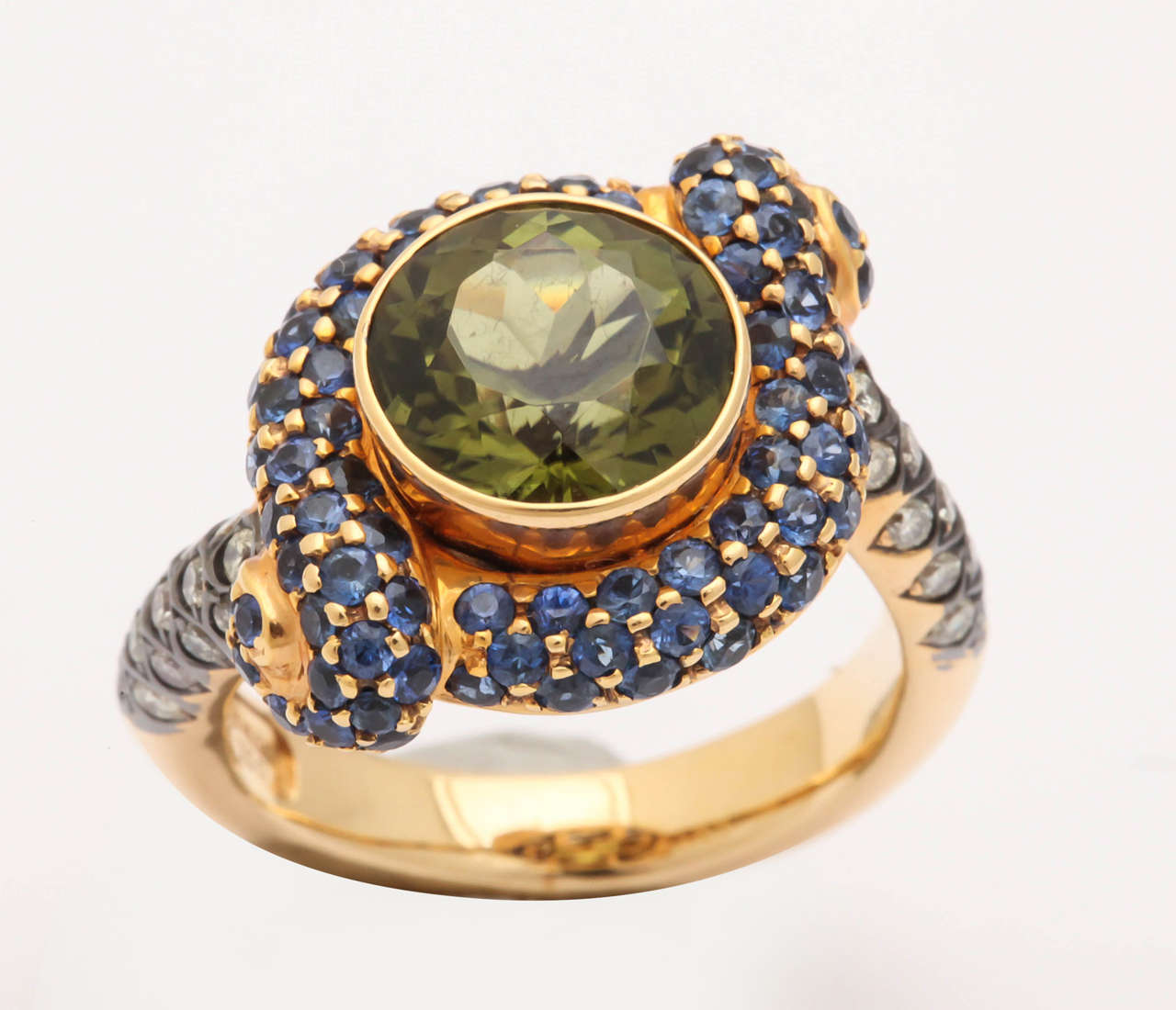 This uniquely shaped 'knot' ring is made of 18 kt orange gold. The color is in between rose gold and 18 kt yellow gold and makes the colored stones pop.
The center round green tourmaline is 3.67 ct, round sapphires, pave set,1.81 ct and white