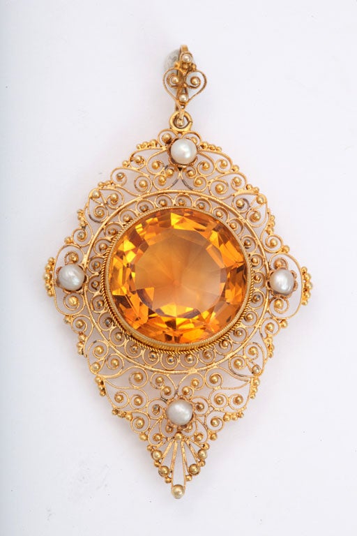 A flame of citrine is beaming sunlike through wisps of gold filigree in this pendant of 12 Ct gold. Like points in an orbit, pearls surround the stone on all sides. This is a lacy pendant, sizable yet delicate. Edwardian jewels were designed