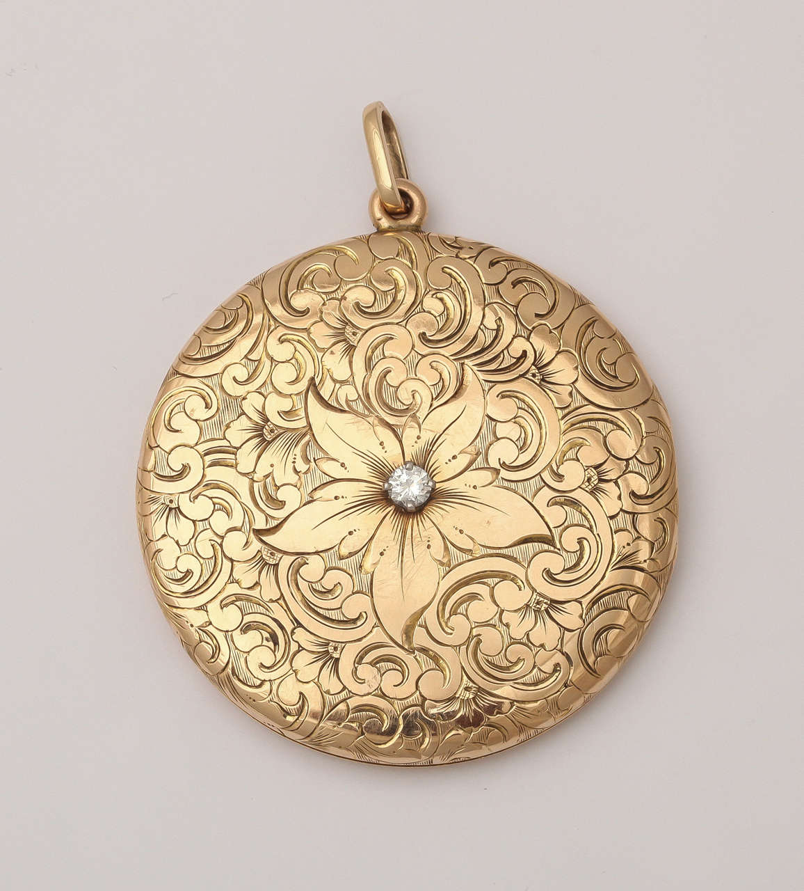 An outstanding locket in size and design created in 14kt gold with florid engraving,. The grand pendant needs no embellishment but has one with the addition of a diamond set in the central large flower.  On the back is a fancy scrolling, more an