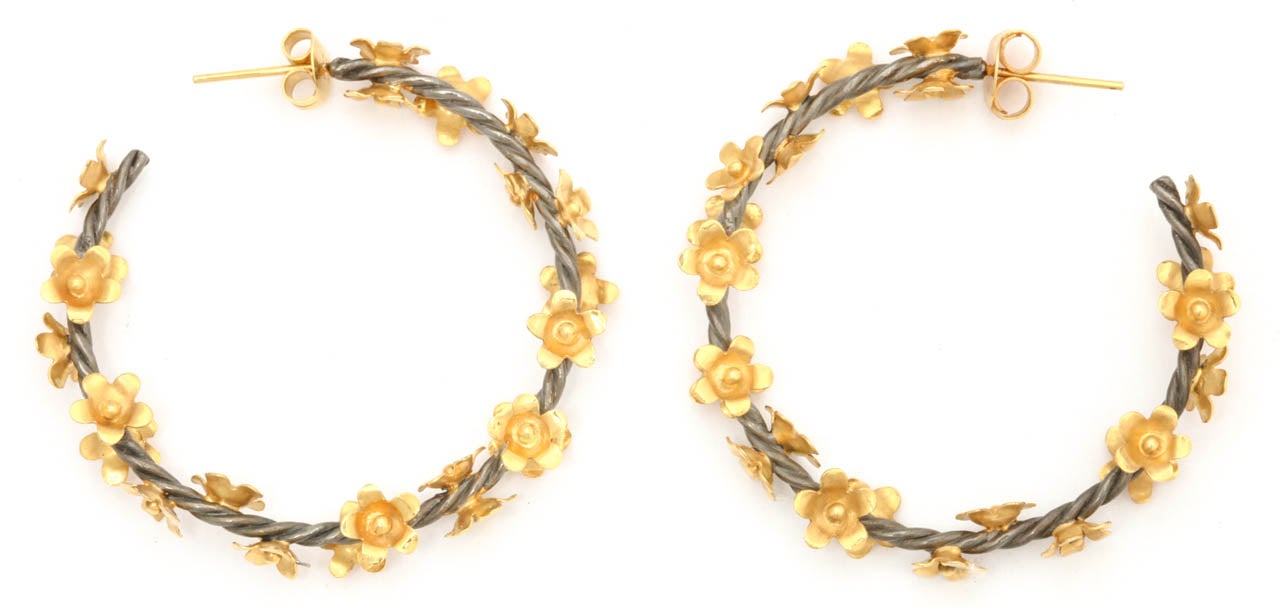 A pair of rhodium plated sterling silver twisted vine hoop earrings with scattered 18kt yellow gold flowers.
Width 1.50 inches