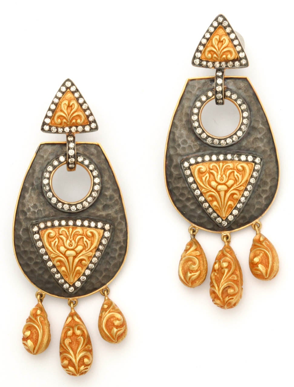 A pair of 18kt yellow gold, rhodium plated sterling silver and diamond earrings. The earrings are composed of hand hammered sterling silver shields which have been adorned with 18kt yellow gold decorative floral plaques and diamonds. There are 18kt