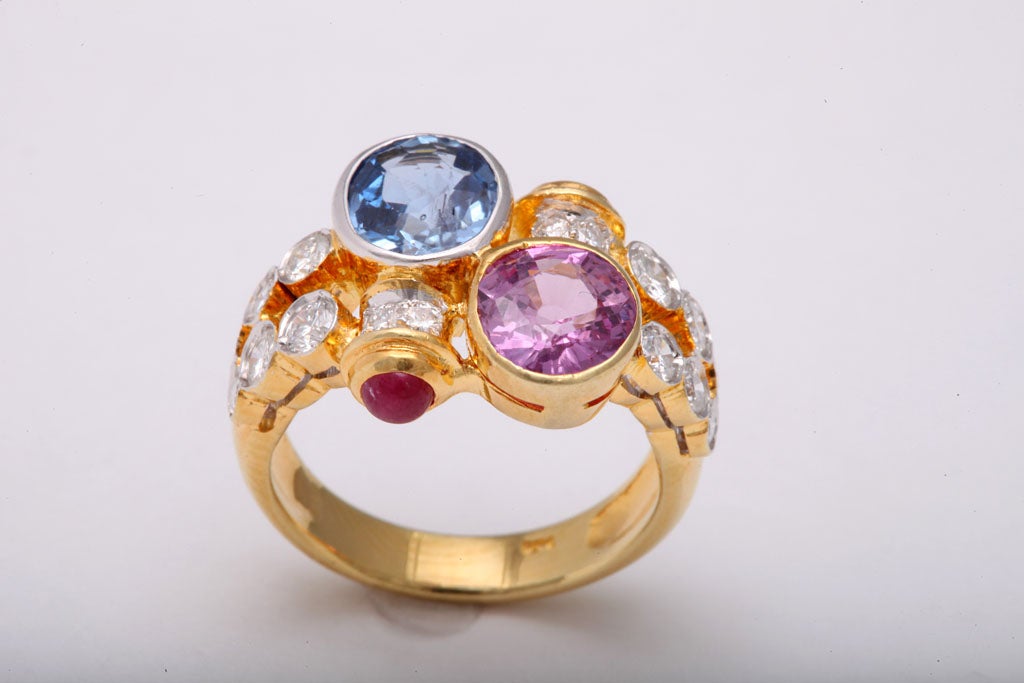 This wonderful ring features two beautiful 2.5c each sapphires, one pink and the other blue.  Accenting these lovely stones are 16 diamonds (1.5 carats approximate total weight) and 2 cab rubies.  The mounting is 18k yellow gold.
The ring size is