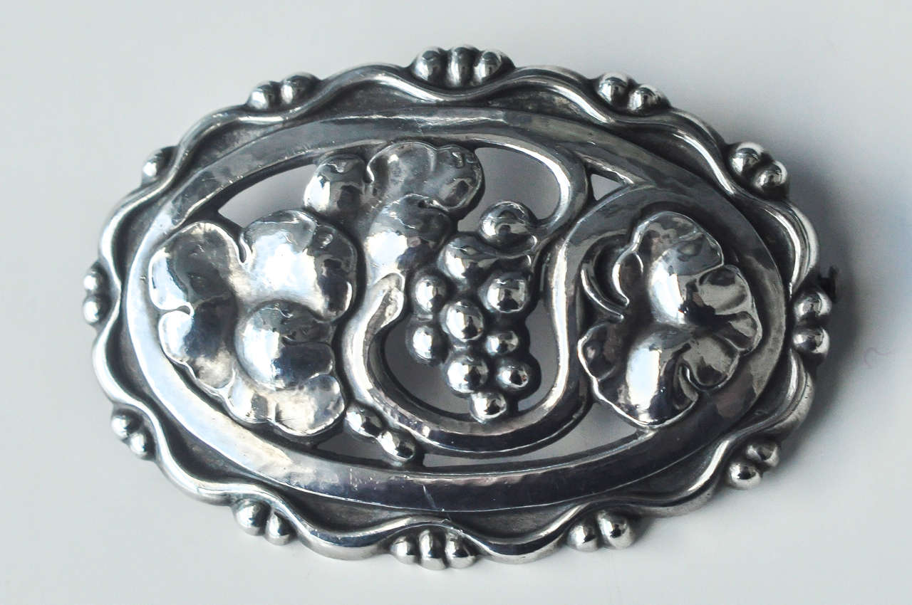 A large, beautifully-designed brooch of stylized, intertwining grapes and leaves with an ornate border.  Dated c. 1933-44.