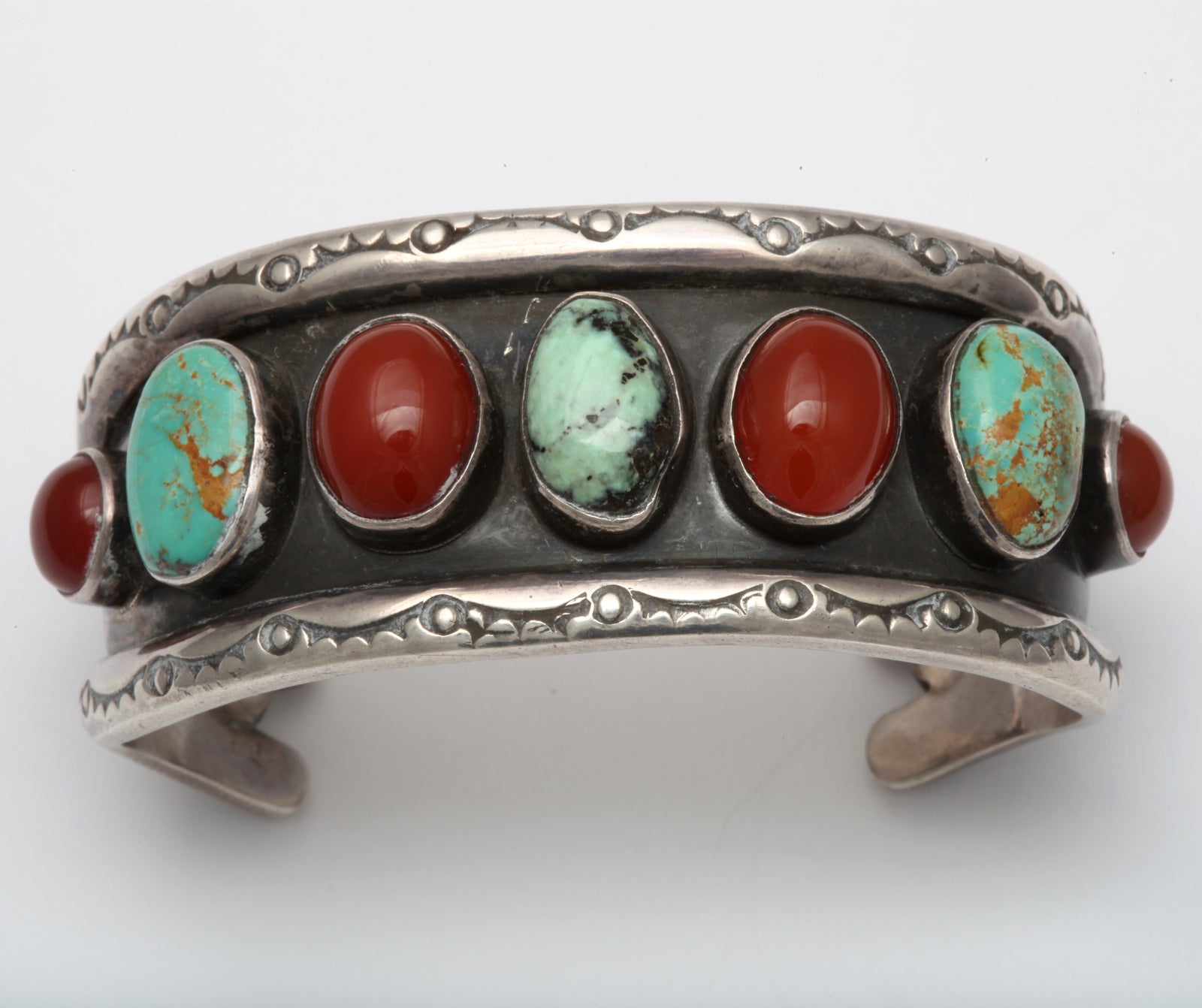 The colors of matrix turquoise and carnelian are a warm and beautiful combination in this hand made Native American cuff from Santa Fe. The stones stand out from their anodized silver background made more dramatic by the natural sterling borders. 