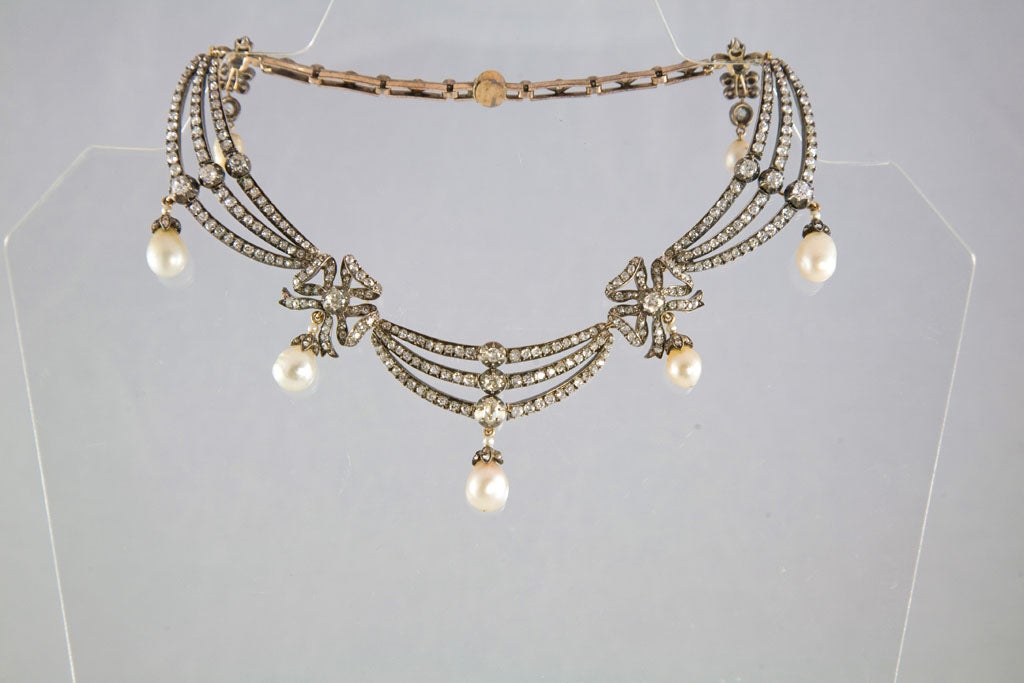 Magnificent necklace is backed in 15 karat gold and topped in silver. It is composed of 3 diamond-set draped sections, each containing 3 rows suspending a natural pearl attached to a diamond-set cap and 1 seed pearl, separated by 2 diamond-set bows,