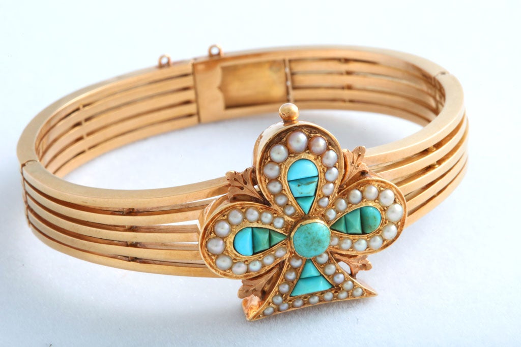 A exquisite example from the Victorian era.  This 18k yellow gold bracelet features exotic cut turquoise pieces surrounded by seed pearls to create a clover motif centrally set on an open 5 row bangle bracelet.  The bracelet hinges open and has a