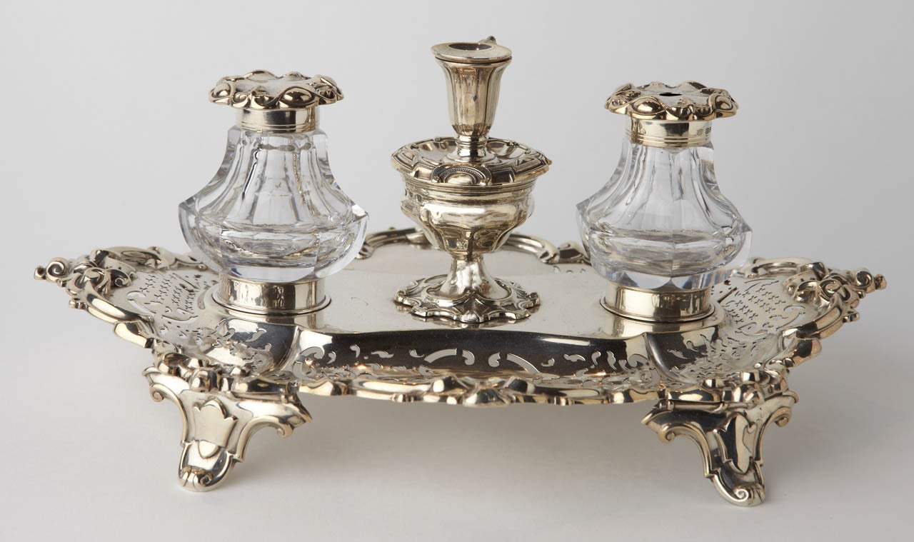 The inkstand with two glass wells has a central wafer box with taperstick.The oval base is  pierced on four feet 
Fully marked Sheffield by H.Wilkinson & co 1853
