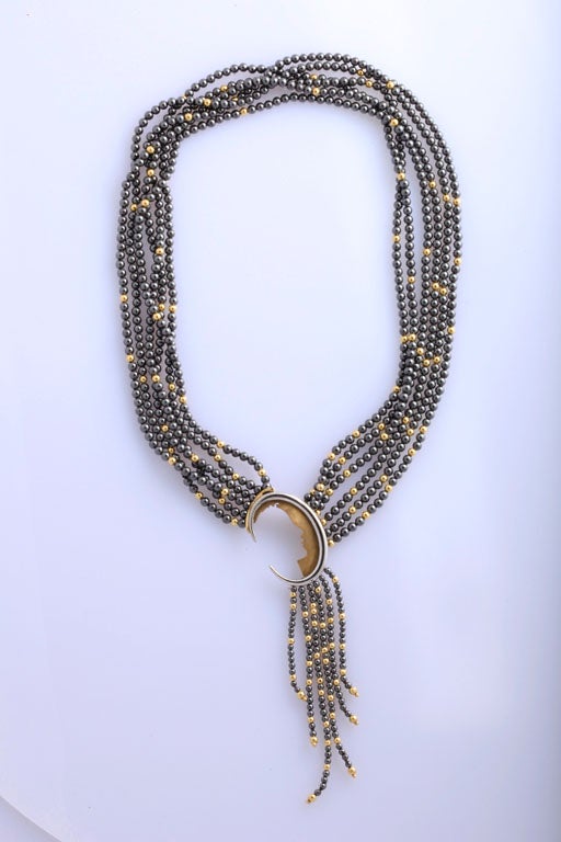 6 Strand necklace designed by Erte and made up of Patinated Sterling Silver   beads interspersed with 14kt Yellow Gold beads. The clasp is a detachable Brooch pendant, which is a profile silhouette  of a woman within a moon shaped crescent &