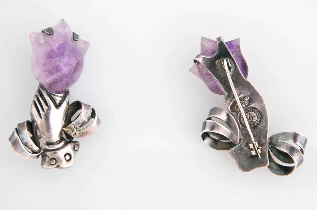 William Spratling is the father of Mexican silversmithing. These pins are a left and right hand holding a flower of amethyst- They are made by hand of
sterling silver. There are two makers marks on the back for  Spratling. 
The amethyst has