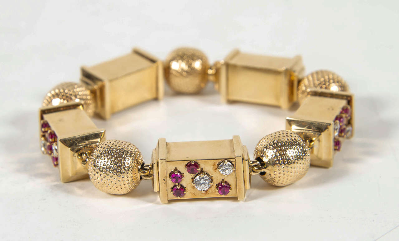 This stunning bracelet features an alternating ball and cylinder design. The ball has a dimple pattern design with alternating cylinders of 14k rose gold set with fine full cut diamonds and rubies of various sizes set in various geometric