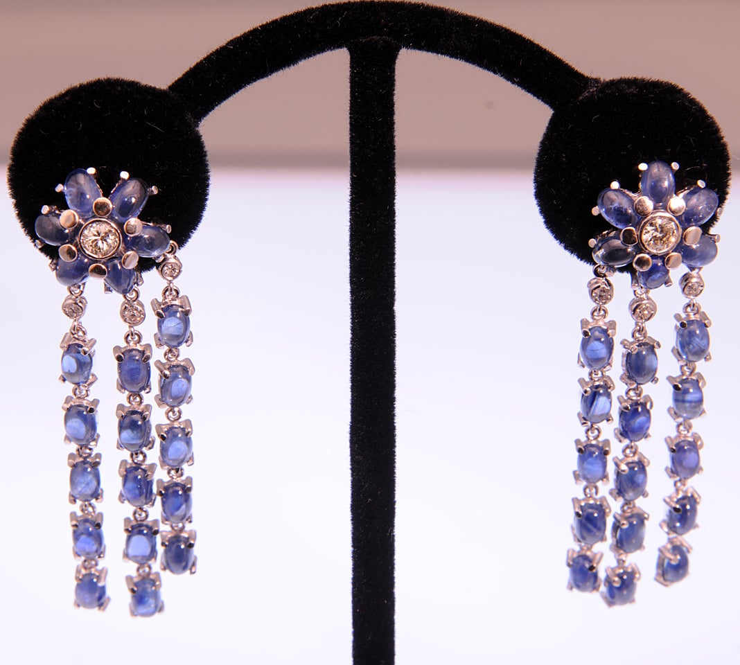 Incredible sapphire and diamond earrings featuring a sapphire flower with a diamond center on the ear with three diamond and sapphire dangling tassels.  These 18k white gold earrings move with the wearer.  They have a post back so the wearer must