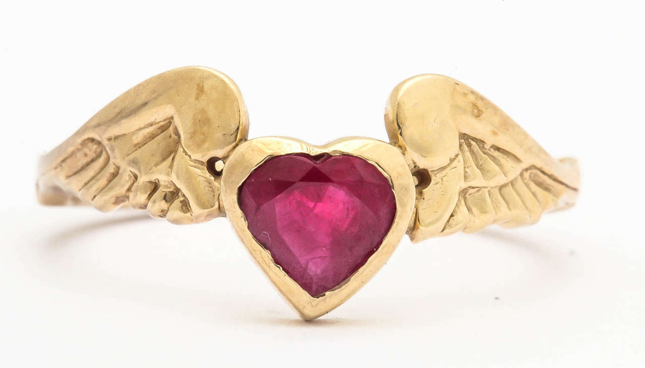 This 18 kt gold ring is bezel set with a 1.1 ct heart shaped ruby. The wings holding the ruby are beautifully carved and detailed and the shank of the ring is engraved all around the back. This ring states that your 