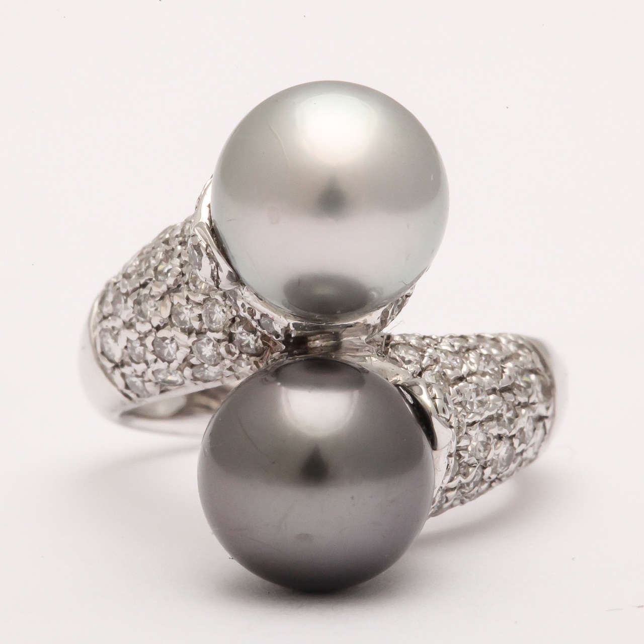 18kt White Gold & Diamond Cross Over Ring set with one Black Pearl & 1 white Pearl.  Each Pearl measuring approximately 8.5mm.  Marked as 750 or 18kt Gold.  The shoulders are pave set with clean,white full cut Diamonds and the Pearls are blemish