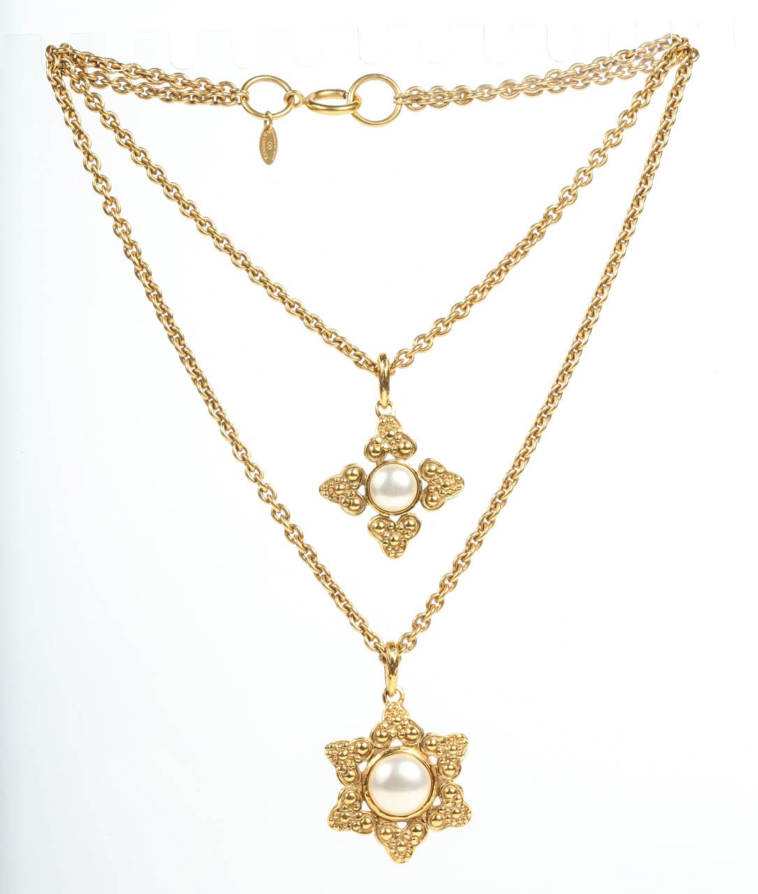A classic double strand necklace by Chanel featuring two pendants with a bubbled trefoil frame around a glass pearl center. Marked on the back of both pendants and with a hang tag on the chain of the 