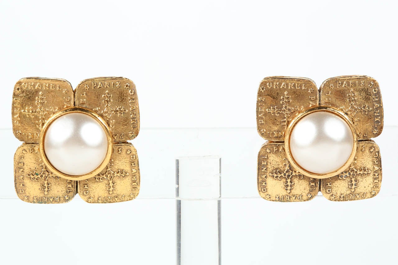 An elegant pair of ear clips by Chanel with a dimpled poured glass pearl set atop four panels of gilt metal with the words 