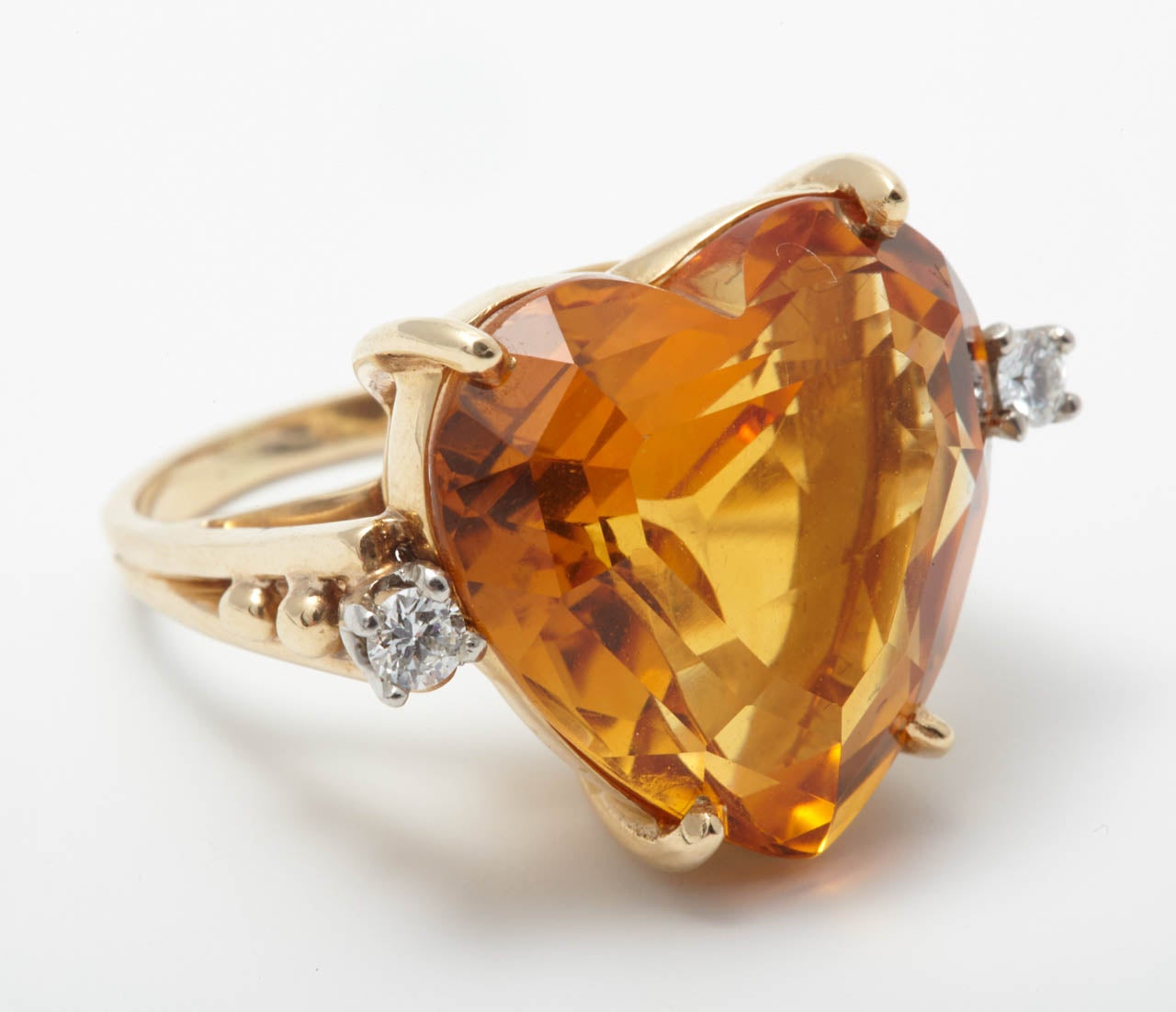 A gold, citrine and diamond dress ring, by Tiffany & Co.
Claw-set with a heart-shaped citrine flanked by a brilliant-cut diamond, weighing approximately 0.15 cts, and bead decoration to the shoulders. 
Engraved Tiffany & Co. Ring sizze is 7 1/4 /