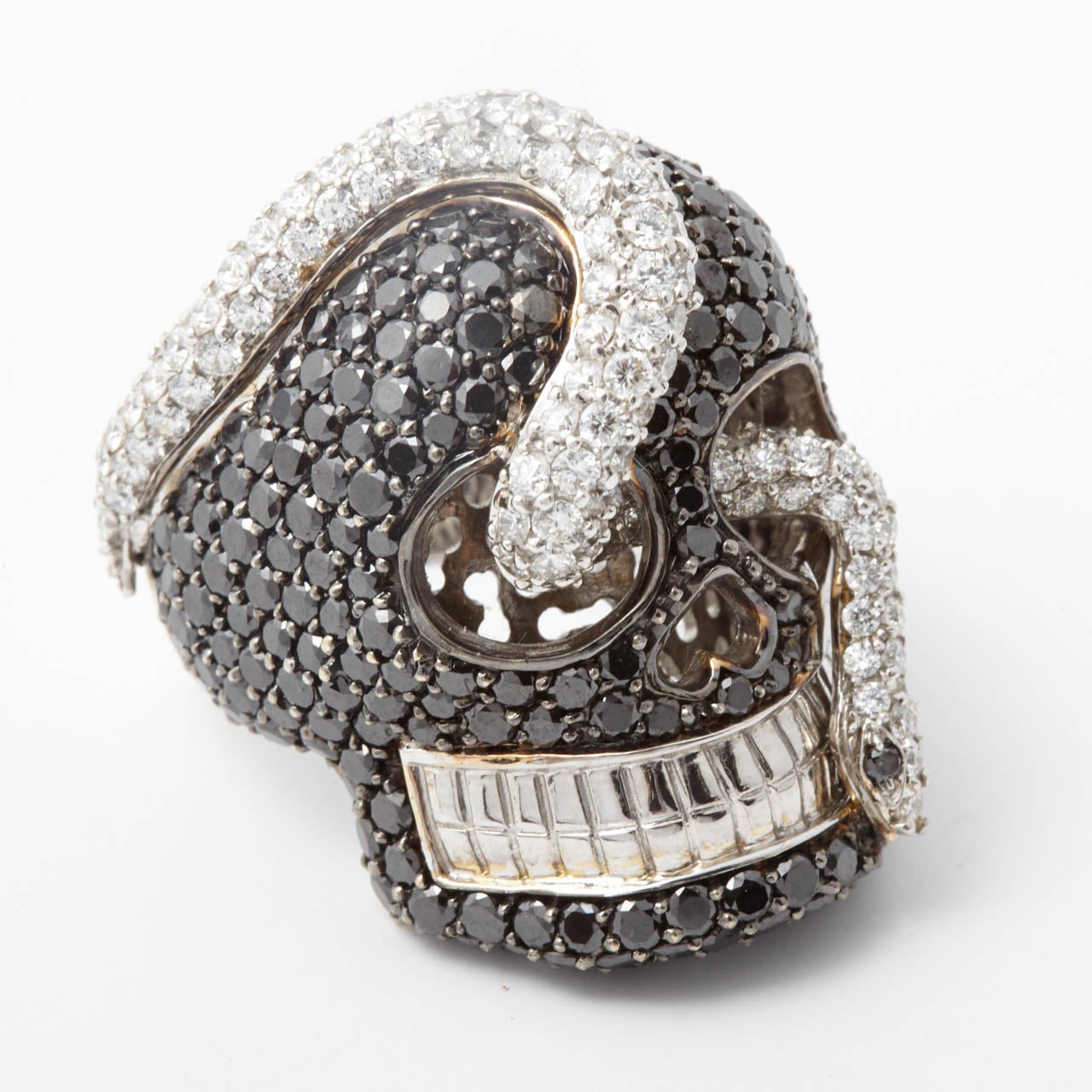 A modern 18K white gold dress ring, designed as a skull, pavé set with brilliant-cut black diamonds, pierced by a pavé set diamond snake, weighing approximately 5.50 carats. Ring sizze 7.5 - 17 3/4.