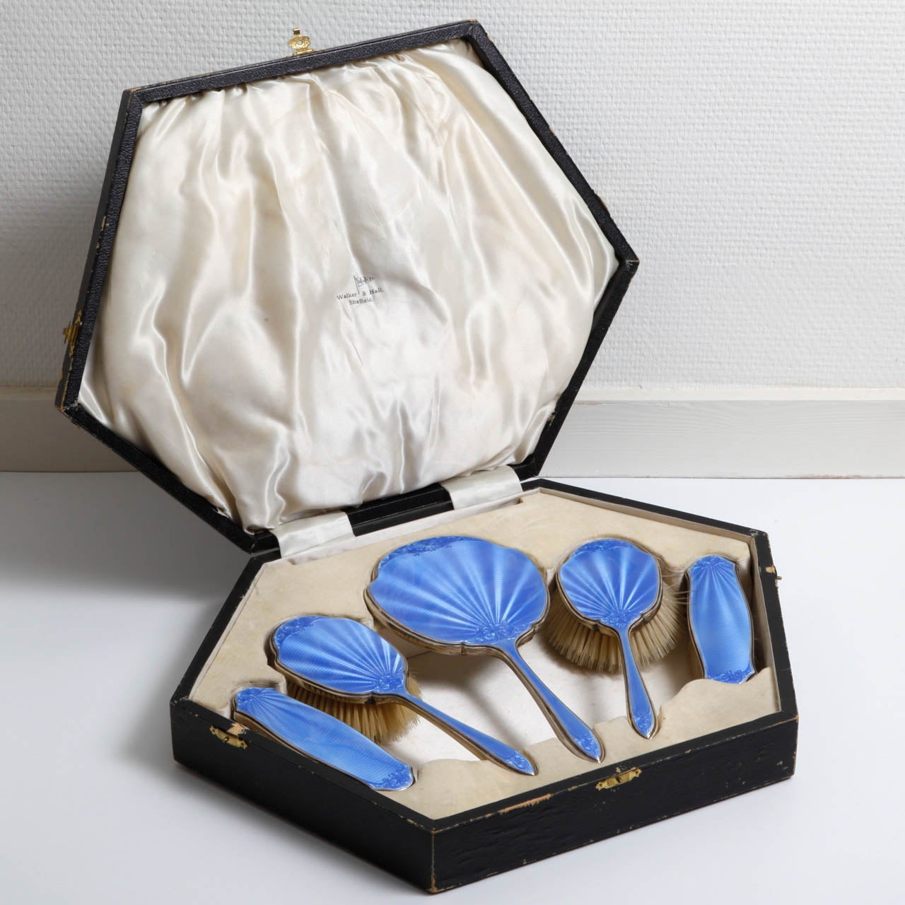 A sterling silver and guillochÃ?© enamel vanity dressing set, by Walker & Hall, comprising of a hand mirror, two hair brushes and two clothing brushes, with mid blue guillochÃ?© enamel and engine turned decoration. Fully hallmarked for Walker &