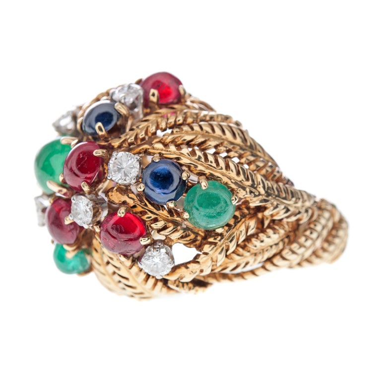 Vibrant colors of cabochon rubies, emeralds, sapphires and brilliant round cut diamonds float and swirl in this delightful dome ring. Warm yellow gold in sculptured floral forms make the rings gallery. Signed David Webb