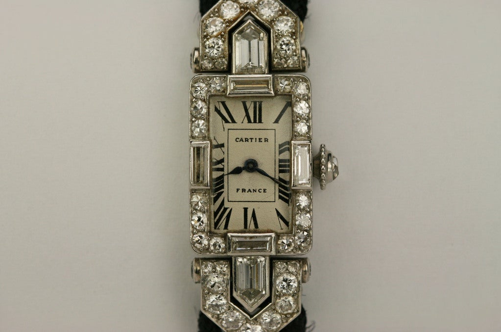 This is an Art Deco diamond and platinum lady's wristwatch by Cartier, France . It appears the case has added length due to the extended lugs. 
The white dial is original with Poires Stuart hands and Roman indexes. This is on a black cord with a