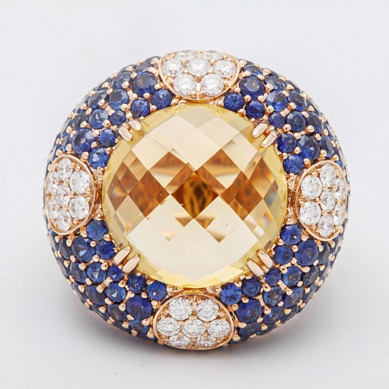 A 18 carat rose gold, citrine, sapphire and diamond dress ring by Arthur Scholl.
Claw-set with a circular rose-cut citrine weighing 11.07 carats, bordered by pavé-set  circular-cut sapphires and brilliant-cut diamonds to the cardinal points, with a