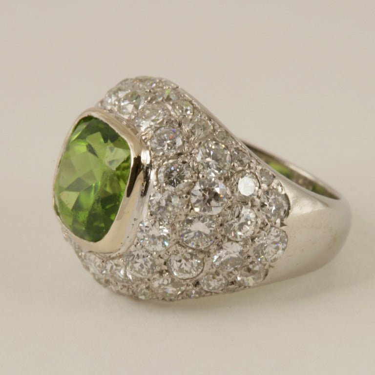 A French Art Deco platinum  ring with peridot and diamonds by René Boivin. The ring centers on a cushion-cut peridot with an approximate weight of 3.25 carats, surrounded by 60 pavé set round-cut diamonds with an approximate total weight of 3.60