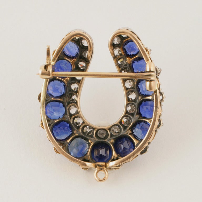 An English Edwardian 15 karat gold horseshoe brooch with sapphires and diamonds. The interior of the horseshoe features 35 cushion-cut sapphires with an approximate total weight of 3.75 carats, 21 old mine-cut diamonds with an approximate total