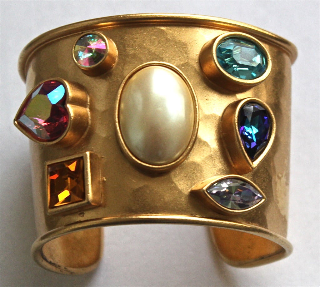 Heavy hammered gilt cuff with vivid glass faceted stones and center pearl from Yves Saint Laurent dating to the 1980's.  Cuff has a curve to it and it is meant to be worn higher up  on the arm. It measures approximately 2.375" on the right side