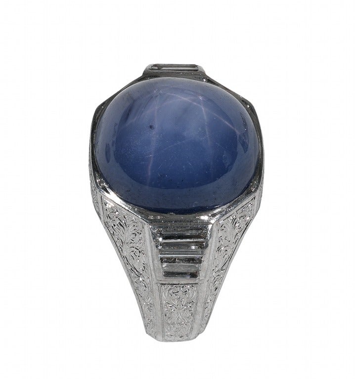 The oval cabochon star sapphire is collet-set, between baguette cut diamond shoulders.

Sapphire - 15mm X 12mm light blue Color (one natural external imperfection), approximate diamond weight 1.20ctw., on an engraved platinum mount decorated with