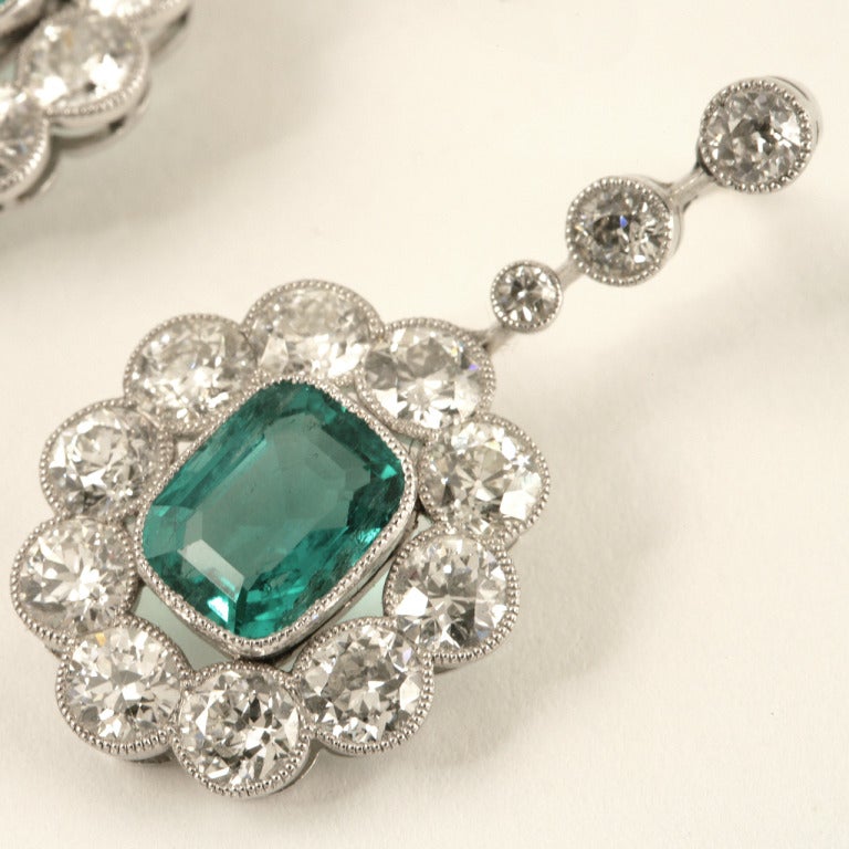 A pair of Edwardian platinum ear pendants with emeralds and diamonds. The earrings have 2 cushion-cut Colombian emeralds, one with an approximate total weight of 3.85 carats, and the other cushion-cut emerald with an approximate total weight of 3.60