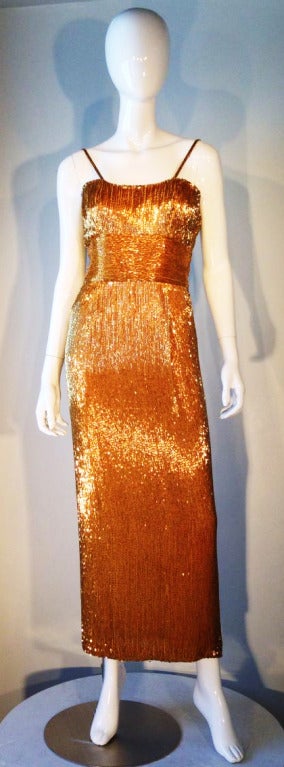 A fine vintage evening column gown from Samuel Winston. Silk item fully lined and completely covered in metallic gold glass bugle beads. Boned bodice features matching shoulder straps and zips up back. Stunning.