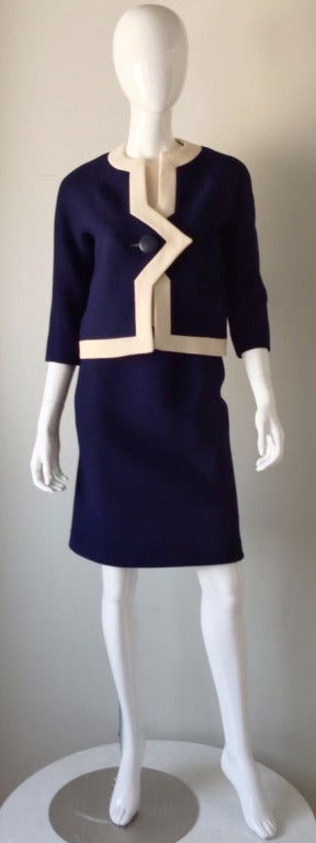 A fine and rare vintage Pierre Cardin haute couture suit. Custom ordered and constructed blue wool item dynamically trimmed in contrasting ivory. Jacket fully lined with single button front. Matching skirt fully lined and zips up back.