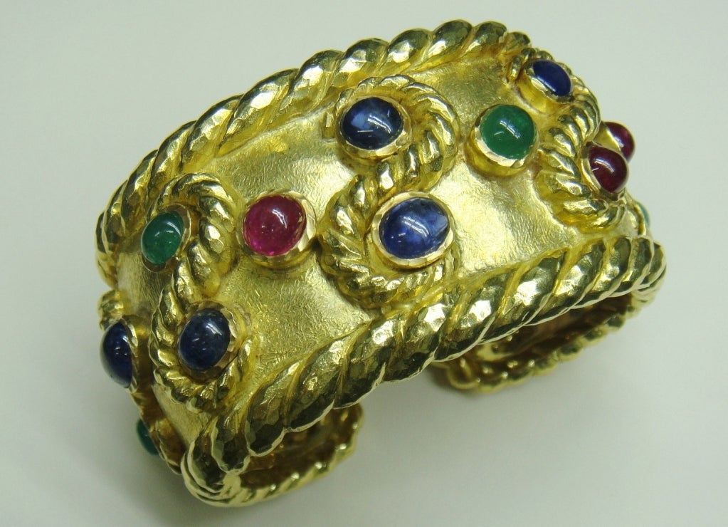 A ruby, sapphire and emerald 18K gold wide cuff. The bracelet includes 6 cabochon emeralds weighing approximately 7.80 carats, 6 rubies weighing approximately 14 carats and 8 sapphires weighing approximately 15 ct. Total weight 150gms