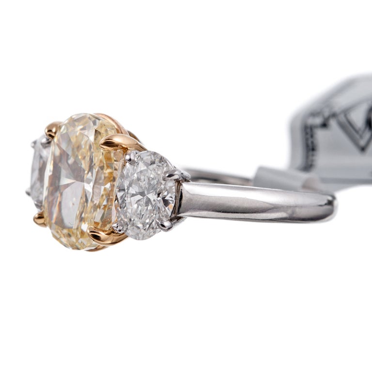 A simple and classic rendition of brilliance: a three stone oval diamond ring with a 2.54ct fancy yellow diamond, flanked by two oval white diamonds. The center stone exhibits Vvs2-Vs1 clarity and the two side diamonds weigh a combined .96 carats,