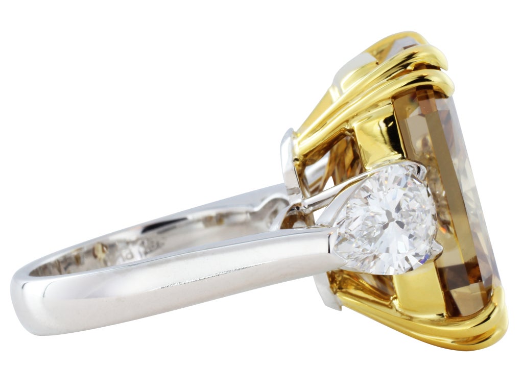 One platinum and 18 karat yellow gold three stone ring consisting of 1 radiant cut natural cognac diamond weighing 20.51 carats, having a color of fancy deep brown-orange/SI2, measuring 17.77 x 13.92 x 9.84 mm with GIA certificate #5111479551 and