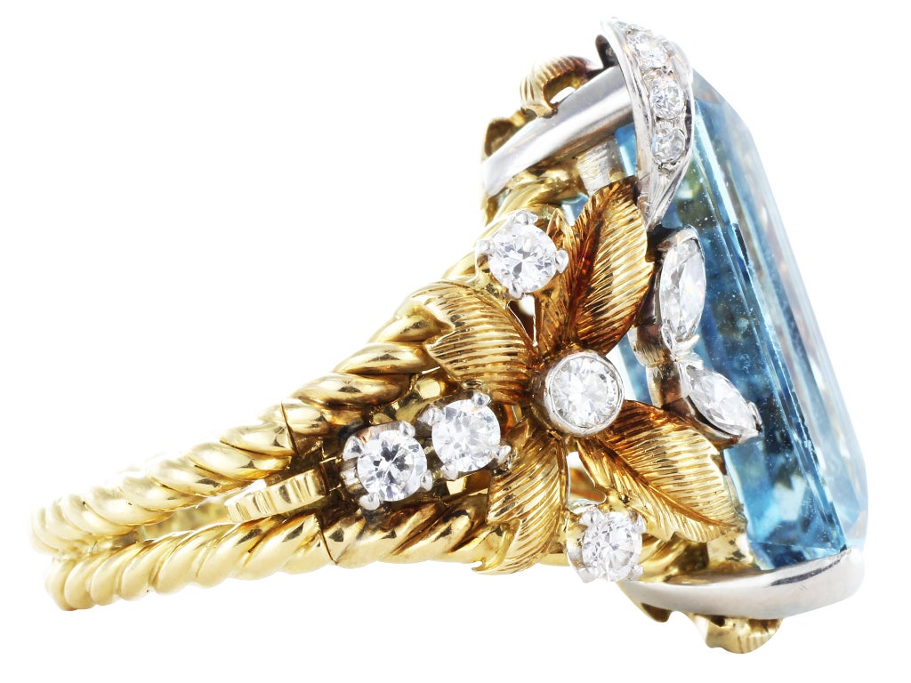 Two tone 18 karat yellow and white gold leaf motif ring consisting of 1 emerald cut aquamarine weighing approximately 17.58 carats, the center stone is set with full diamond accents in a floral motif open work mounting, signed E. Serafini.